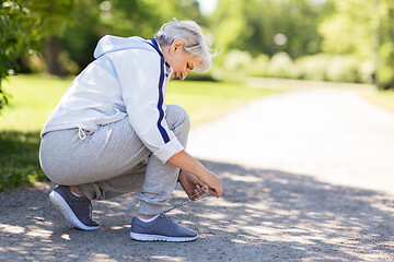 Image showing senior woman tying sport shoe laces at summer park