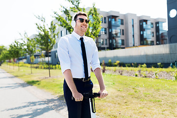 Image showing businessman with headphones riding scooter in city