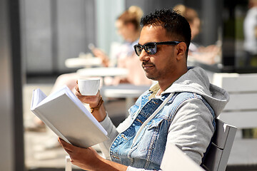 Image showing man reading book and drinking coffee at city cafe