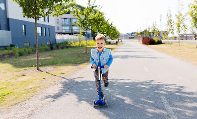 Image showing happy little boy riding scooter in city