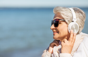 Image showing old woman in headphones listens to music on beach