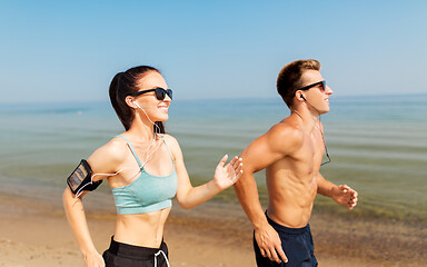 Image showing couple with phones and arm bands running on beach