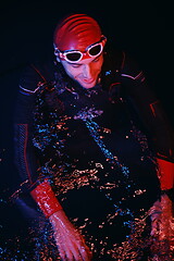 Image showing authentic triathlete swimmer having a break during hard training on night neon gel light