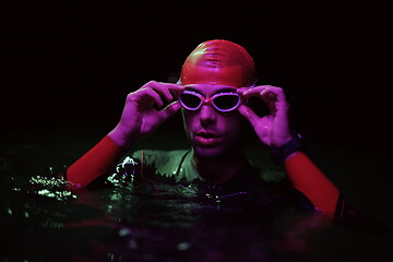 Image showing authentic triathlete swimmer having a break during hard training on night neon gel light