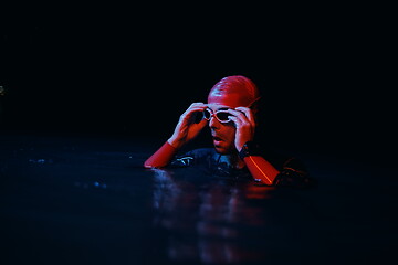 Image showing authentic triathlete swimmer having a break during hard training on night neon gel light