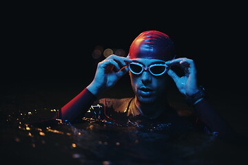 Image showing authentic triathlete swimmer having a break during hard training on night neon gel light