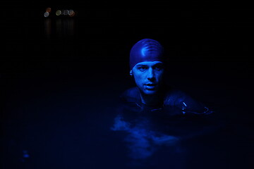 Image showing authentic triathlete swimmer having a break during hard training on night neon gel light