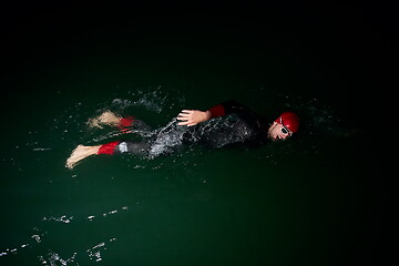 Image showing triathlon athlete swimming in dark night wearing wetsuit