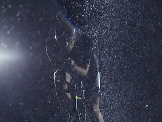 Image showing triathlon athlete riding bike on rainy night