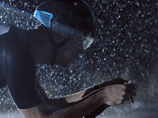 Image showing triathlon athlete riding bike on rainy night