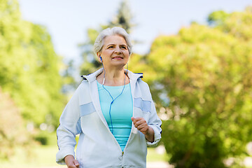 Image showing senior woman with earphones running in summer park