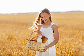 Image showing girl with bread and milk in basket on cereal field