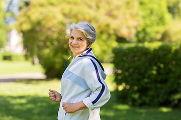 Image showing senior woman with earphones running in summer park