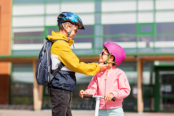 Image showing school boy fastening girl\'s helmet for scooter