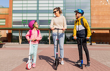 Image showing happy school children with mother riding scooters