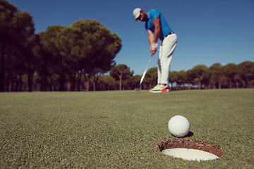 Image showing golf player hitting shot, ball on edge of hole