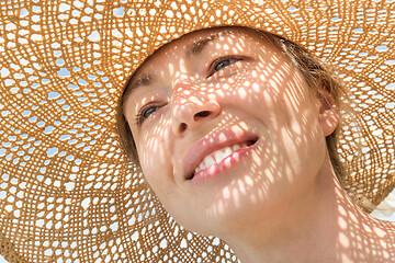 Image showing Close-up portrait of woman wearing straw hat enjoying summer sun. Pattern of shadows falling on her face