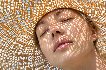 Image showing Close-up portrait of woman, eyes shut, wearing straw hat enjoying summer sun. Pattern of shadows falling on her face