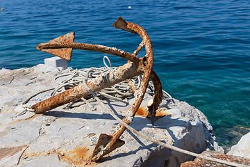 Image showing Old rusty anchor on rock by blue sea