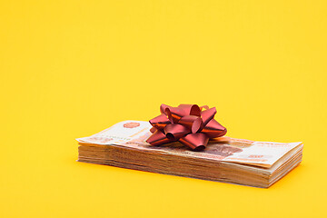 Image showing On the bundle of five thousandth bills lies a red bow, yellow background