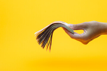 Image showing Hand holds out a wad of money, yellow background