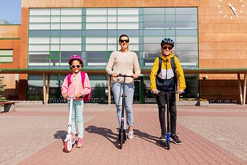 Image showing happy school children with mother riding scooters