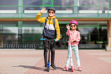 Image showing happy school children in helmets riding scooters