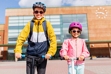 Image showing happy school children in helmets riding scooters