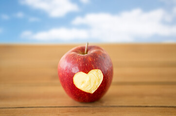 Image showing red apple with carved heart shape on wooden table