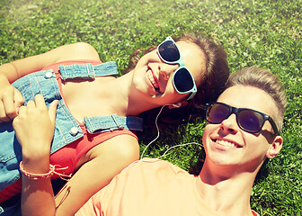 Image showing happy teenage couple with earphones lying on grass