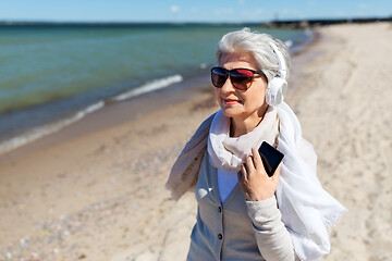 Image showing old woman in headphones with smartphone on beach