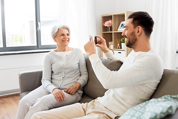 Image showing adult son photographing senior mother at home