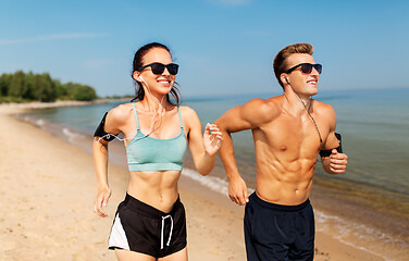 Image showing couple with phones and arm bands running on beach