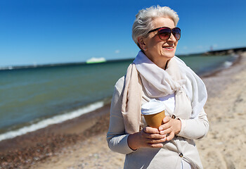 Image showing senior woman drinking takeaway coffee on beach
