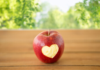 Image showing red apple with carved heart shape on wooden table