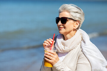 Image showing senior woman drinking orange juice on beach