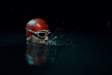 Image showing authentic triathlete swimmer having a break during hard training on night neon gel light