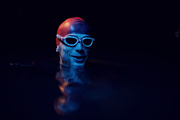 Image showing authentic triathlete swimmer having a break during hard training on night neon gel light