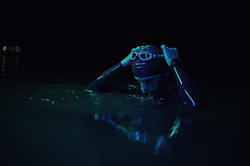 Image showing authentic triathlete swimmer having a break during hard training on night neon gel light