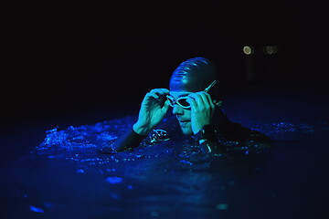 Image showing authentic triathlete swimmer having a break during hard training on night neon gel light