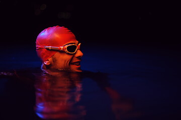 Image showing authentic triathlete swimmer having a break during hard training on night neon gel light