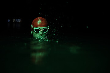 Image showing authentic triathlete swimmer having a break during hard training on night neon gel light