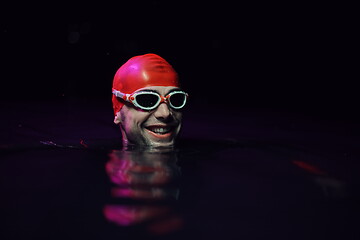 Image showing authentic triathlete swimmer having a break during hard training on night neon gel light