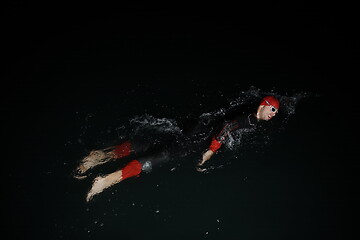 Image showing triathlon athlete swimming in dark night wearing wetsuit