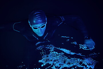 Image showing authentic triathlete swimmer having a break during hard training on night neon gel light