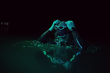 Image showing authentic triathlete swimmer having a break during hard training on night neon gel light