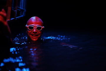 Image showing authentic triathlete swimmer having a break during hard training on night neon gel light