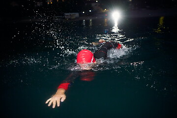 Image showing triathlon athlete swimming in dark night wearing wetsuit