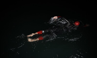 Image showing triathlon athlete swimming in dark night wearing wetsuit