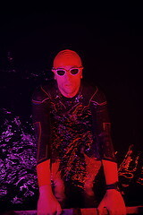 Image showing authentic triathlete swimmer having a break during hard training on night neon gel light